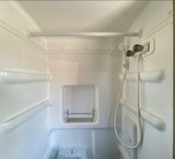 Explore this compact RV rental shower/bathroom. Features a shower head, toilet, and shelving for essentials.