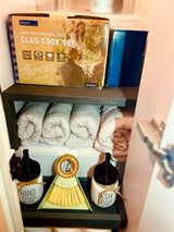 Compact Clad Cook Set, rolled towels, hand/dish soap, and cleaning brush stored in neat shelves for an RV rental.