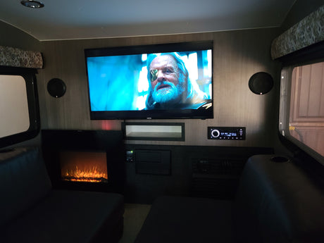 Enjoy an RV rental's cozy entertainment setup: TV displaying a movie, electric fireplace, and stereo.
