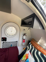 Compact RV rental interior: bed, round door, fire extinguisher, & storage net, perfect for cozy adventures.