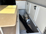 RV rental interior: practical under-bench storage with Kilmat insulation, a black bag, and clean white cabinets.
