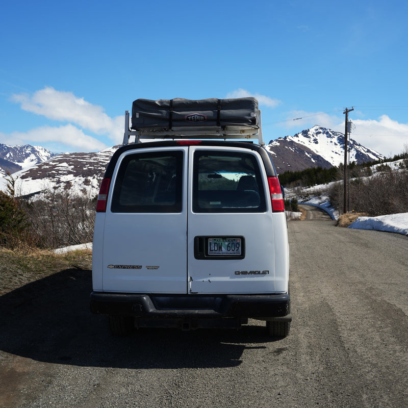 White cargo van RV rental with rooftop tent on a scenic gravel road in snowy Alaskan mountains under blue sky. — photo 7