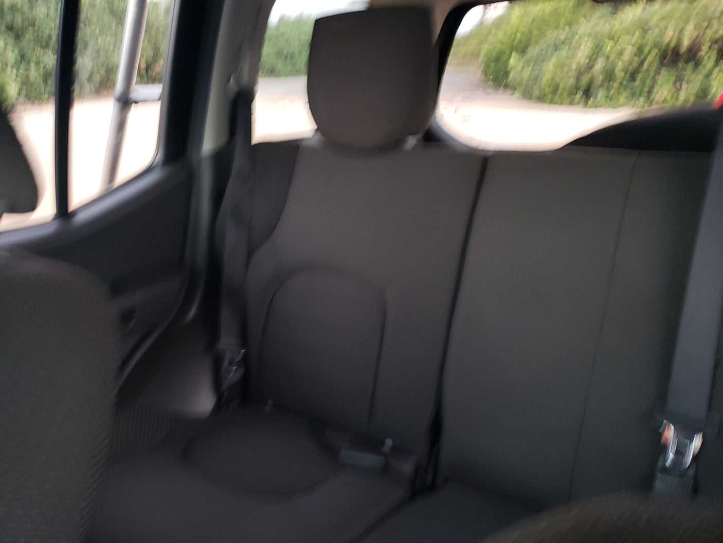 RV rental: Interior view of dark rear seats and visible seatbelts. Outside, a dirt road and green trees.