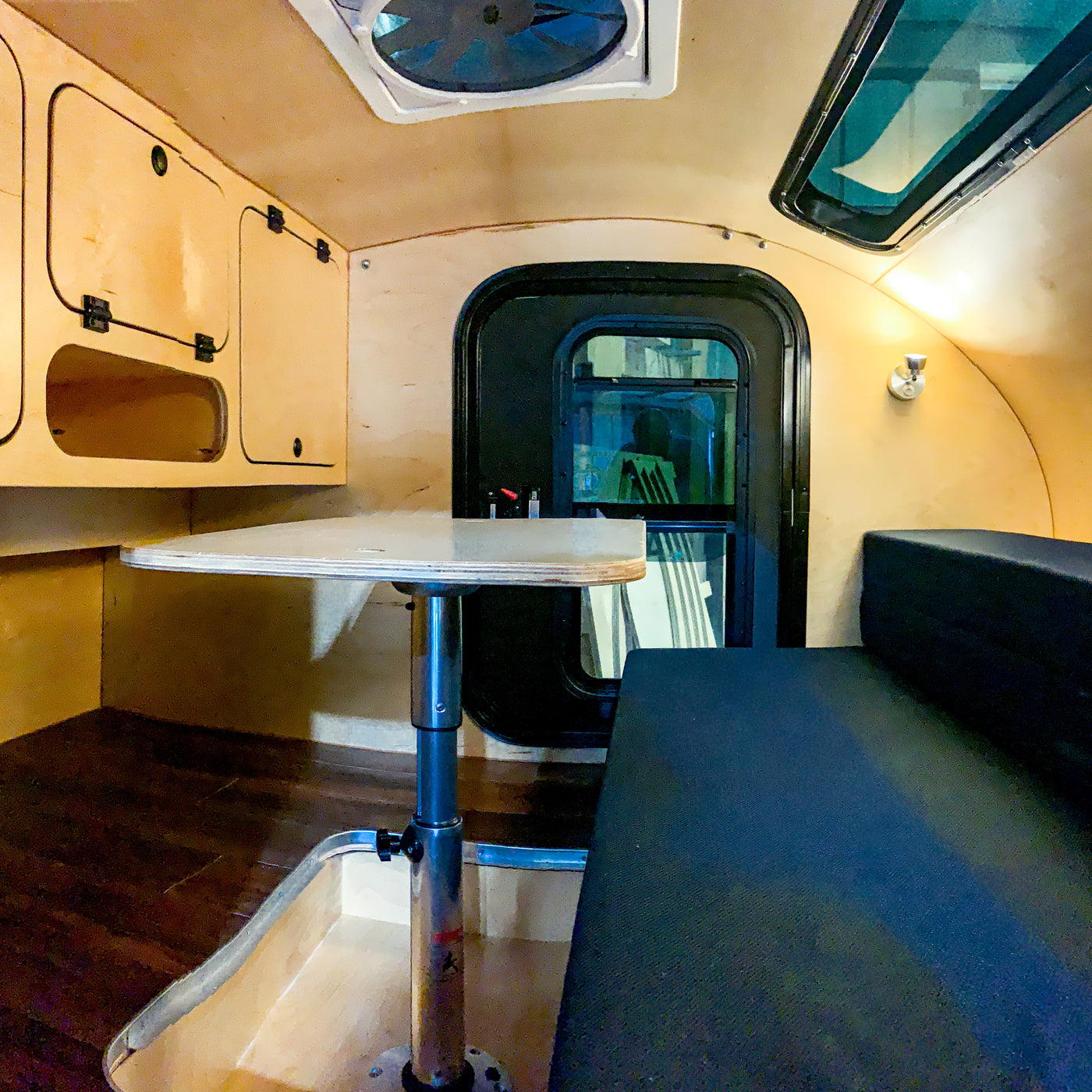 RV rental interior featuring light wood cabinets, an adjustable table, and black bench seating. Overhead vent and window add light. — photo 4