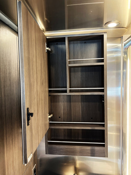 RV rental interior: open wood grain cabinet with multiple shelves and white retention bars for secure storage.