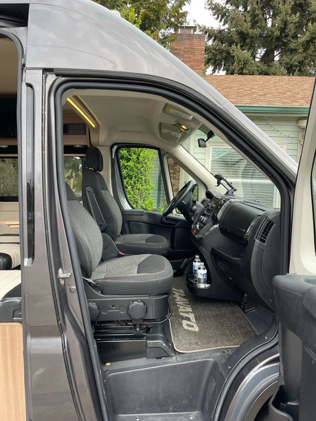 Step inside this Travato RV rental: the front cabin view shows driver and passenger seats, dashboard, and interior lighting from the open door.