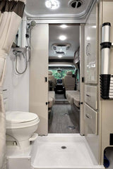 This RV rental features a compact bathroom with toilet & shower, and an open layout view into the living and driver's cab.