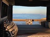 Ocean view from an RV rental: a cozy bed overlooking calm waters, flying birds, and distant waves. Van life travel.