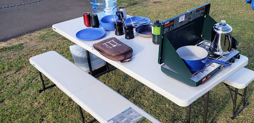 RV rental adventure! Portable stove, kettle, and dishes on a folding picnic table, perfect for outdoor cooking.