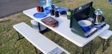 RV rental adventure! Portable stove, kettle, and dishes on a folding picnic table, perfect for outdoor cooking.