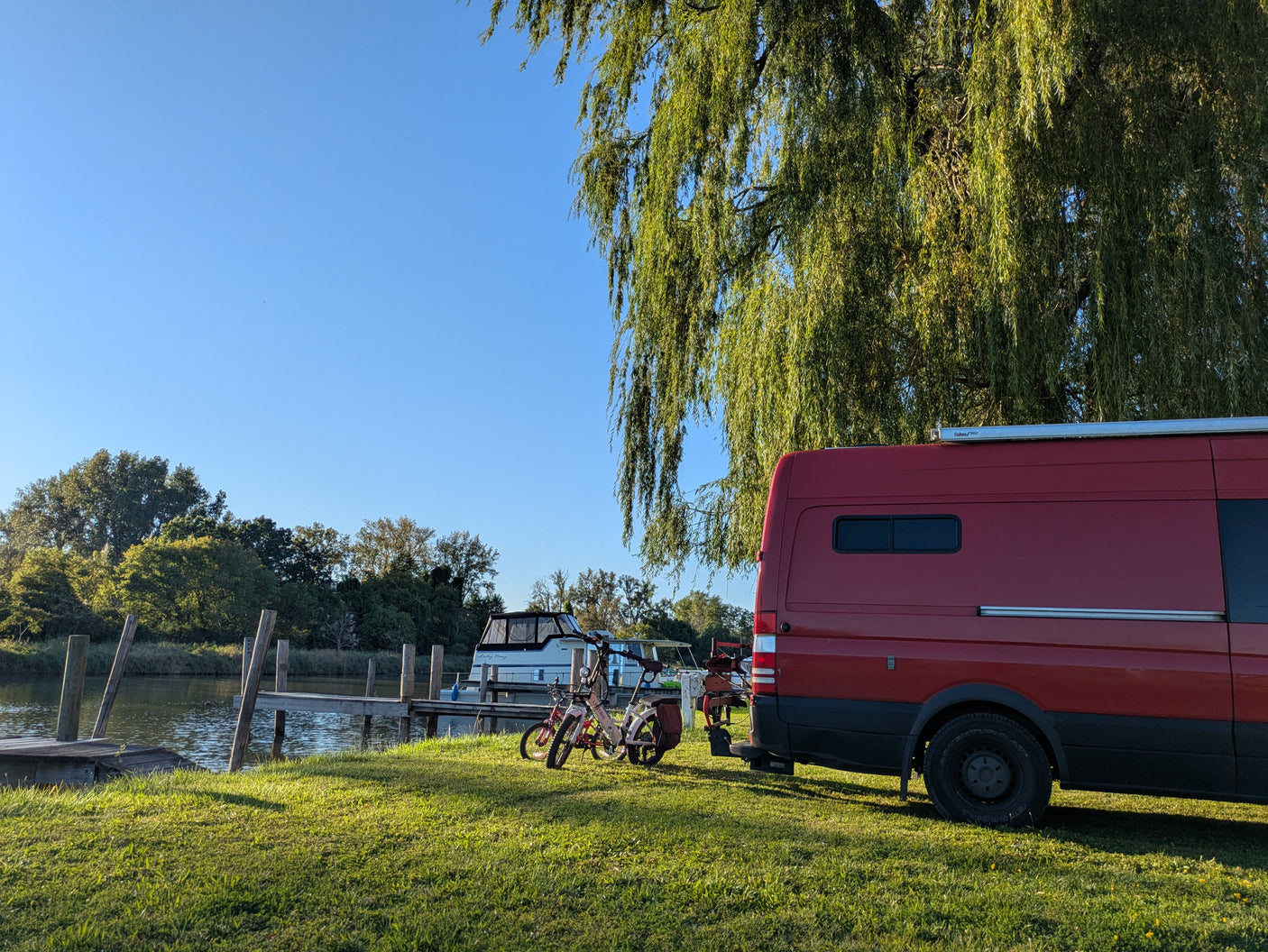 Scenic rv rental setup: Red camper van, bikes, and boat "Lady May" by a tranquil waterway and green trees.