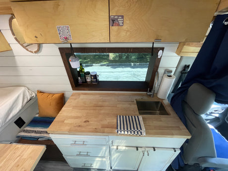 Cozy RV rental interior with a compact kitchen, wooden counter, sink, and overhead cabinets, perfect for van life adventures.