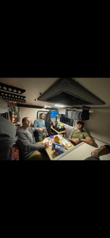Four men share a meal at a table inside a compact, well-lit rv rental camper, featuring a heater. Perfect for travel adventures.
