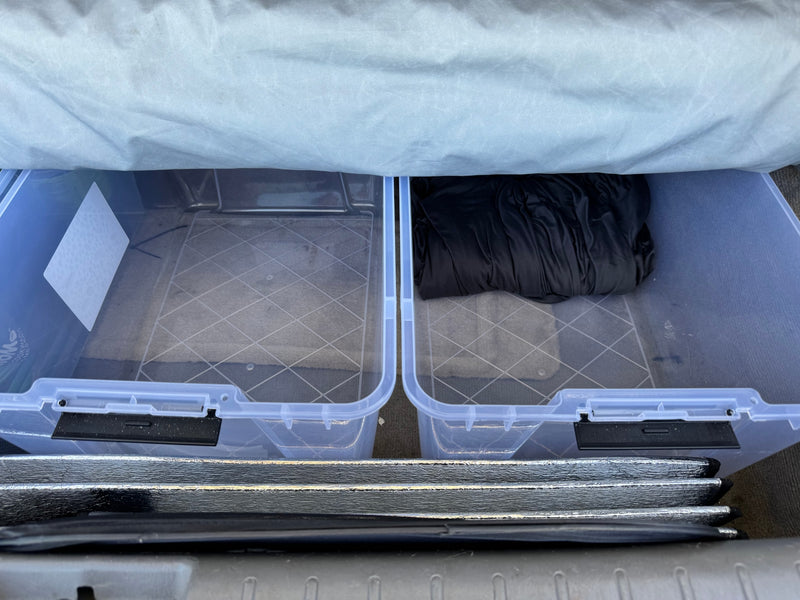 RV rental storage setup: clear bins holding travel gear, a black jacket, and reflective sunshades. — photo 9