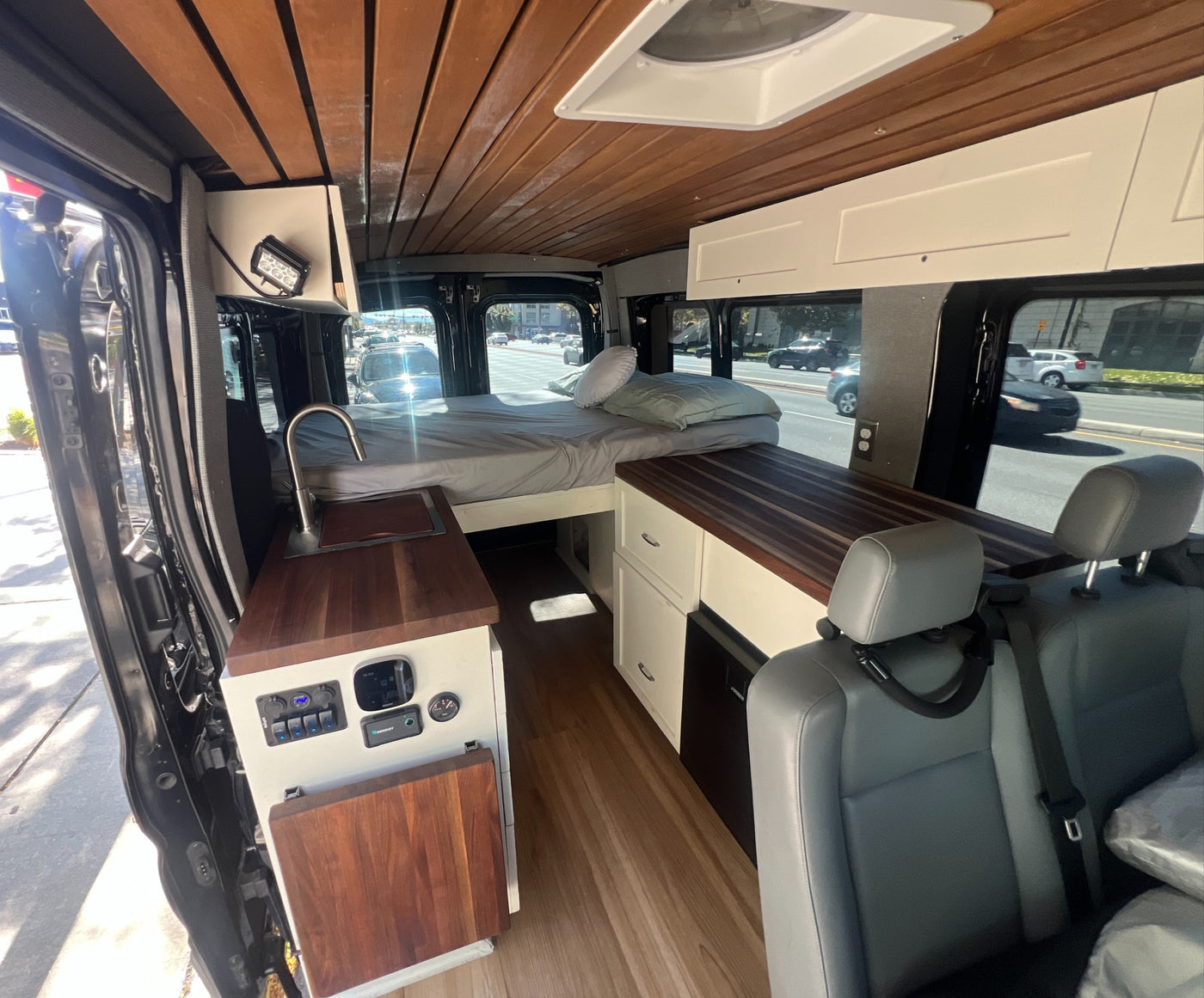 Interior of a modern rv rental camper van, featuring a cozy bed, kitchenette, wood ceiling, and ample storage. — photo 8