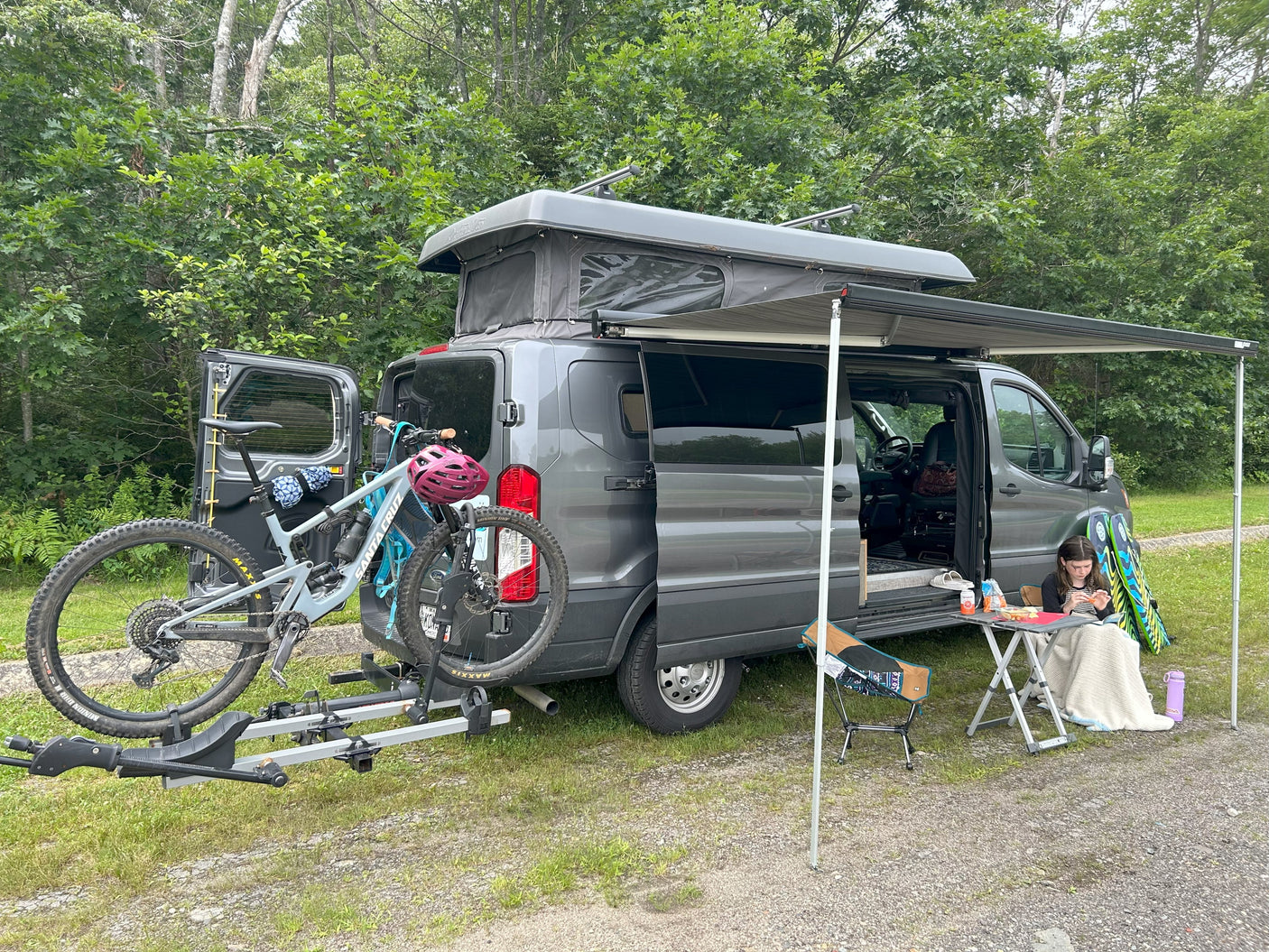 Pop-top RV rental with bikes on a hitch rack and an extended awning, offering a comfy outdoor camping setup for relaxation.