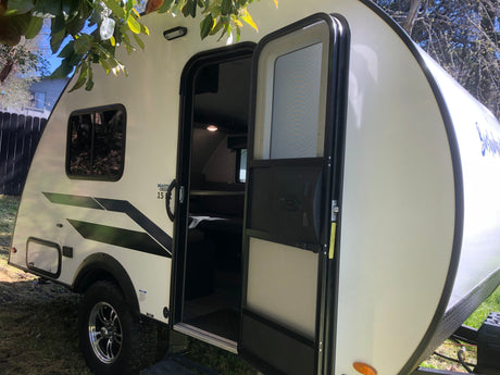 White teardrop RV rental, a compact travel trailer parked outdoors with its door open, ready for adventure.