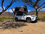 White SUV with a Roofnest roof-top tent deployed, parked by mountains. Explore nature with this convenient rv rental.