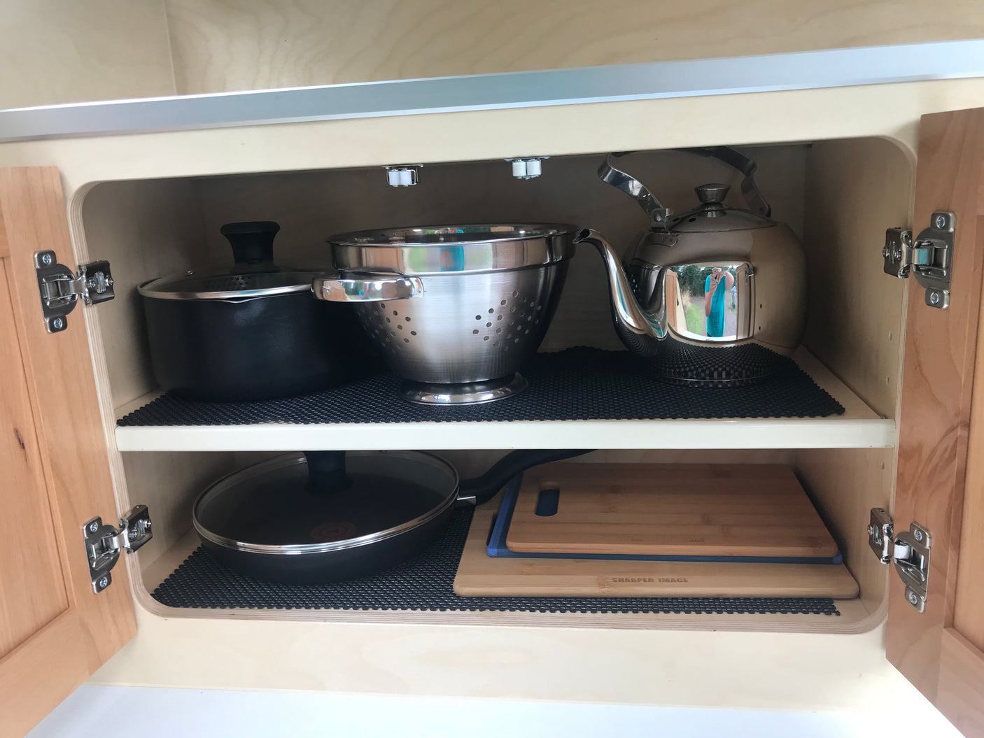 Organized RV rental cabinet shows pots, pans, a kettle, colander, and cutting boards on anti-slip mats.