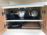 Organized RV rental cabinet shows pots, pans, a kettle, colander, and cutting boards on anti-slip mats.