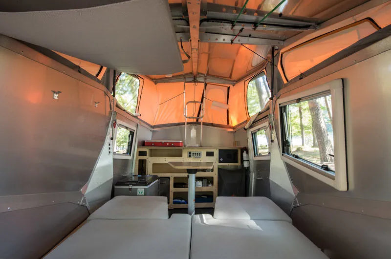  parked in a sunny wooded campsite.|Camping in style! An orange SUV tows a blue pop-top Cricket camper in a sunny pine forest. Consider this RV rental for your next trip.|An illuminated Taxa Cricket RV rental with its orange pop-up roof — photo 2