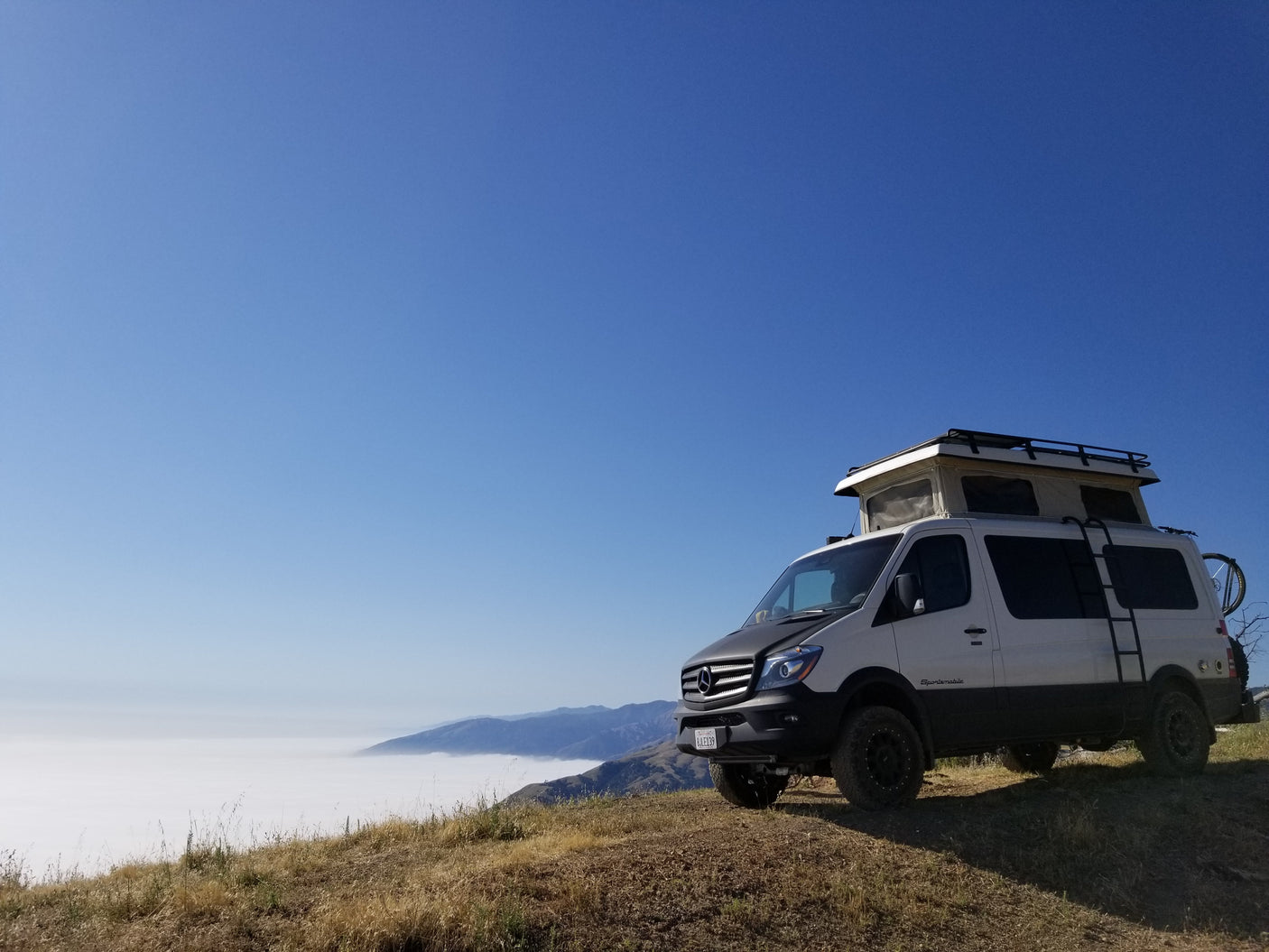 White Sportsmobile Sprinter camper van perched above a foggy mountain landscape, ideal for an RV rental adventure.