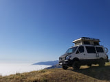 White Sportsmobile Sprinter camper van perched above a foggy mountain landscape, ideal for an RV rental adventure.