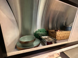 Compact and organized kitchenware storage in an RV rental, featuring dishes, containers, and a basket for easy travel.