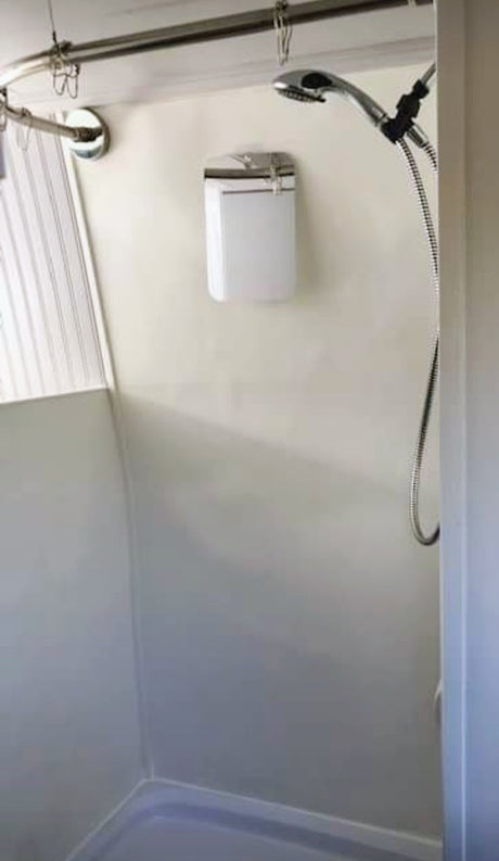 An RV rental shower featuring a compact design, curved curtain rod, handheld showerhead, and a wall-mounted dispenser.