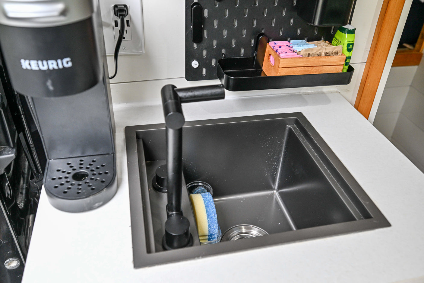 Modern RV rental kitchen with a black Keurig, sink, and pegboard for organized essentials, including sugar packets.