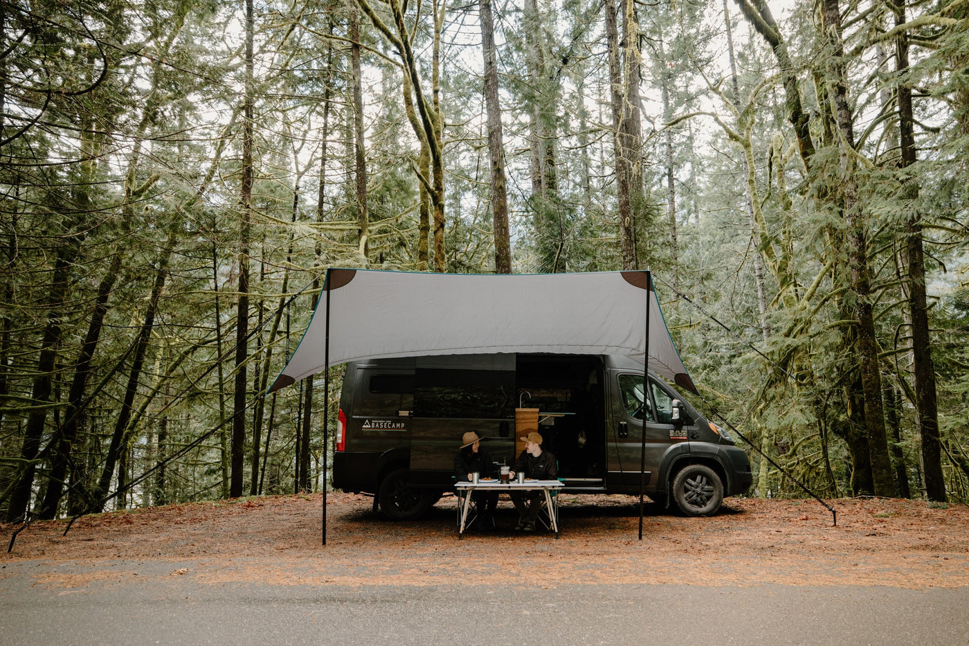 RV rental campervan with an extended awning, two people dining at a table in a mossy forest. — photo 16