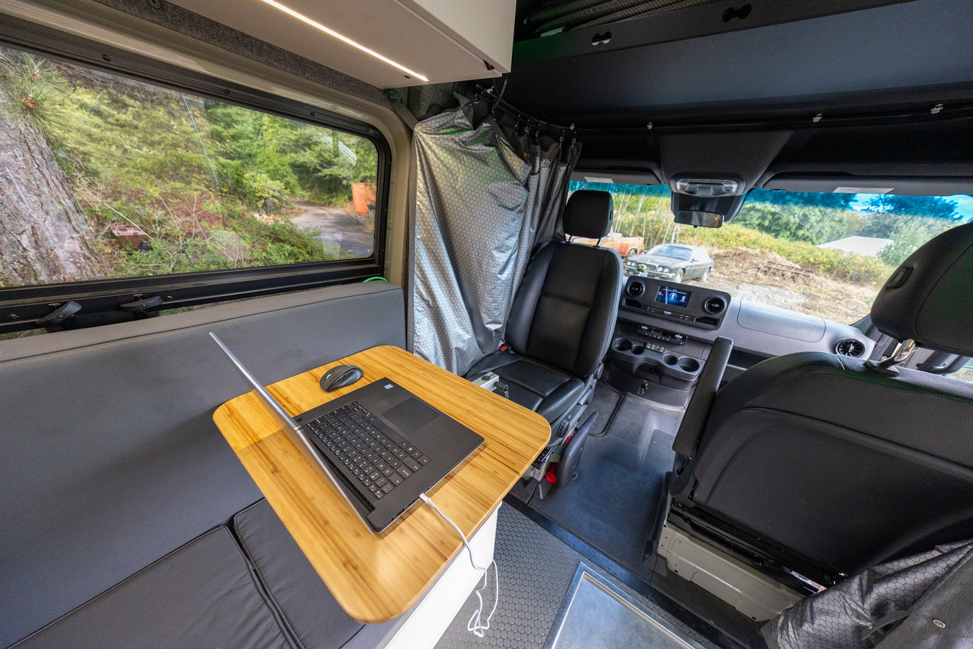 RV rental interior features a functional mobile office with a laptop, comfy bench, window view, and shower area.