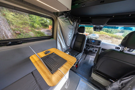 RV rental interior features a functional mobile office with a laptop, comfy bench, window view, and shower area.