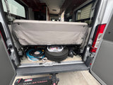 This RV rental's camper van interior reveals rear storage, showing a spare tire, hoses, and peeling seat upholstery.