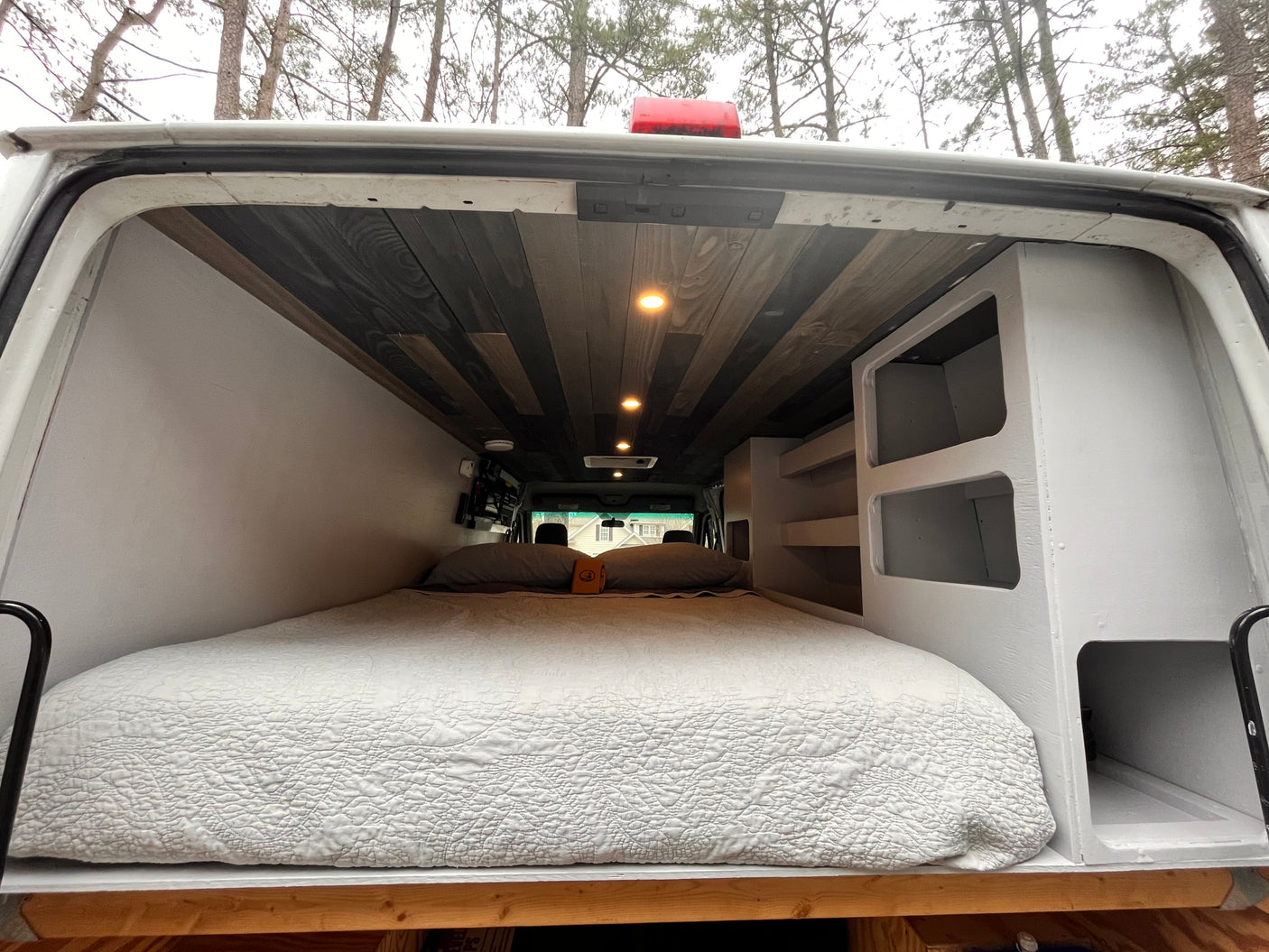 Inside an rv rental van conversion: a cozy bed under a stylish wood plank ceiling with spotlights & built-in storage units.