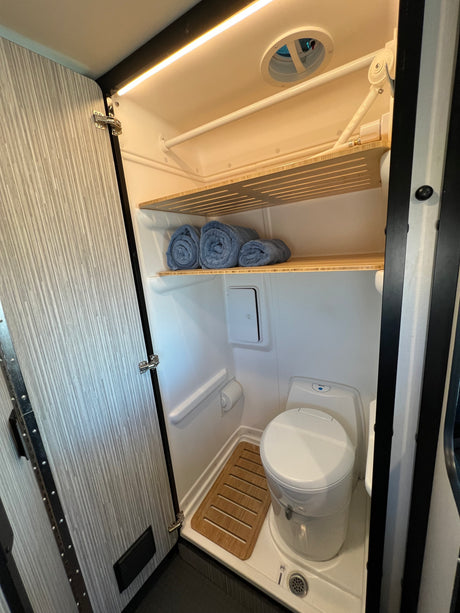 RV rental wet bath: toilet, shower pan, bamboo shelves with towels, overhead light & vent. Compact & functional.
