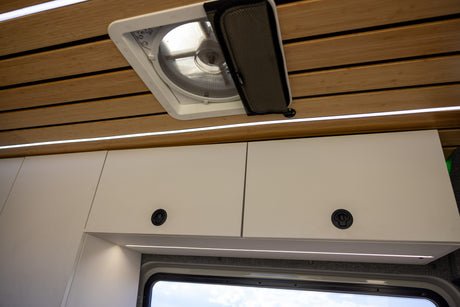 Modern RV rental interior showing a wood-slatted ceiling, ceiling fan, LED lighting, and white overhead cabinets.