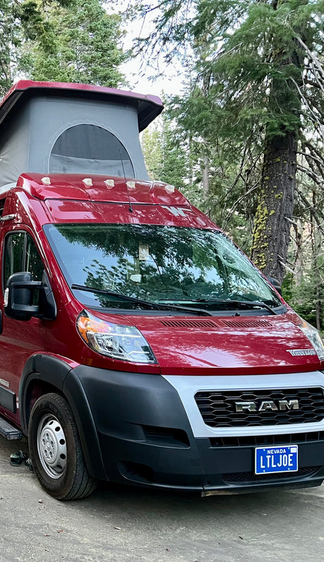 Red Winnebago Ram pop-top camper van (RV rental) parked in a forest. Features include a Nevada plate.