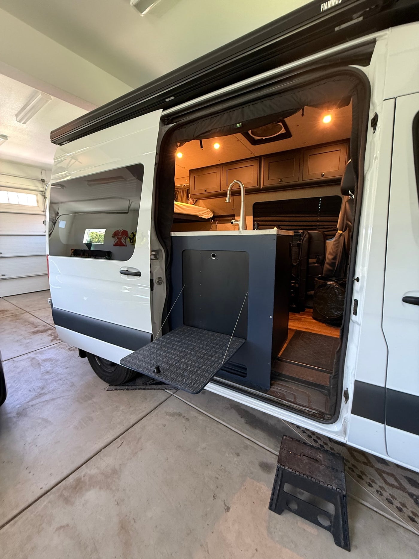 RV rental camper van with open side door revealing interior kitchen, pull-out table, and awning, parked in a garage. — photo 13