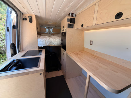 Spacious rv rental interior featuring a wood-paneled van conversion with a kitchenette, bed, and work counter for comfortable travel.