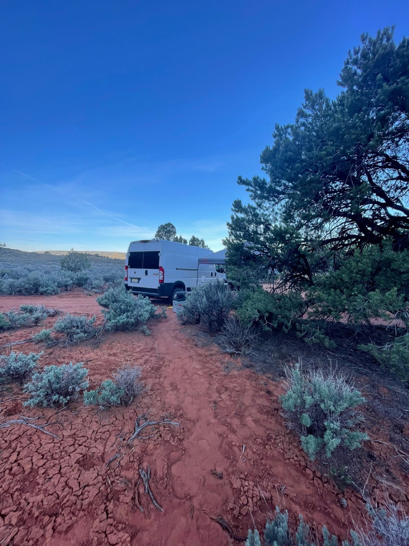 An RV rental camper van is parked for desert camping, with its awning extended, on red cracked earth, surrounded by sparse shrubs. — photo 18