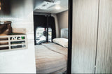Cozy rv rental interior: a comfortable bed with a quilted blanket and pillow, and an AC unit in a compact camper van.