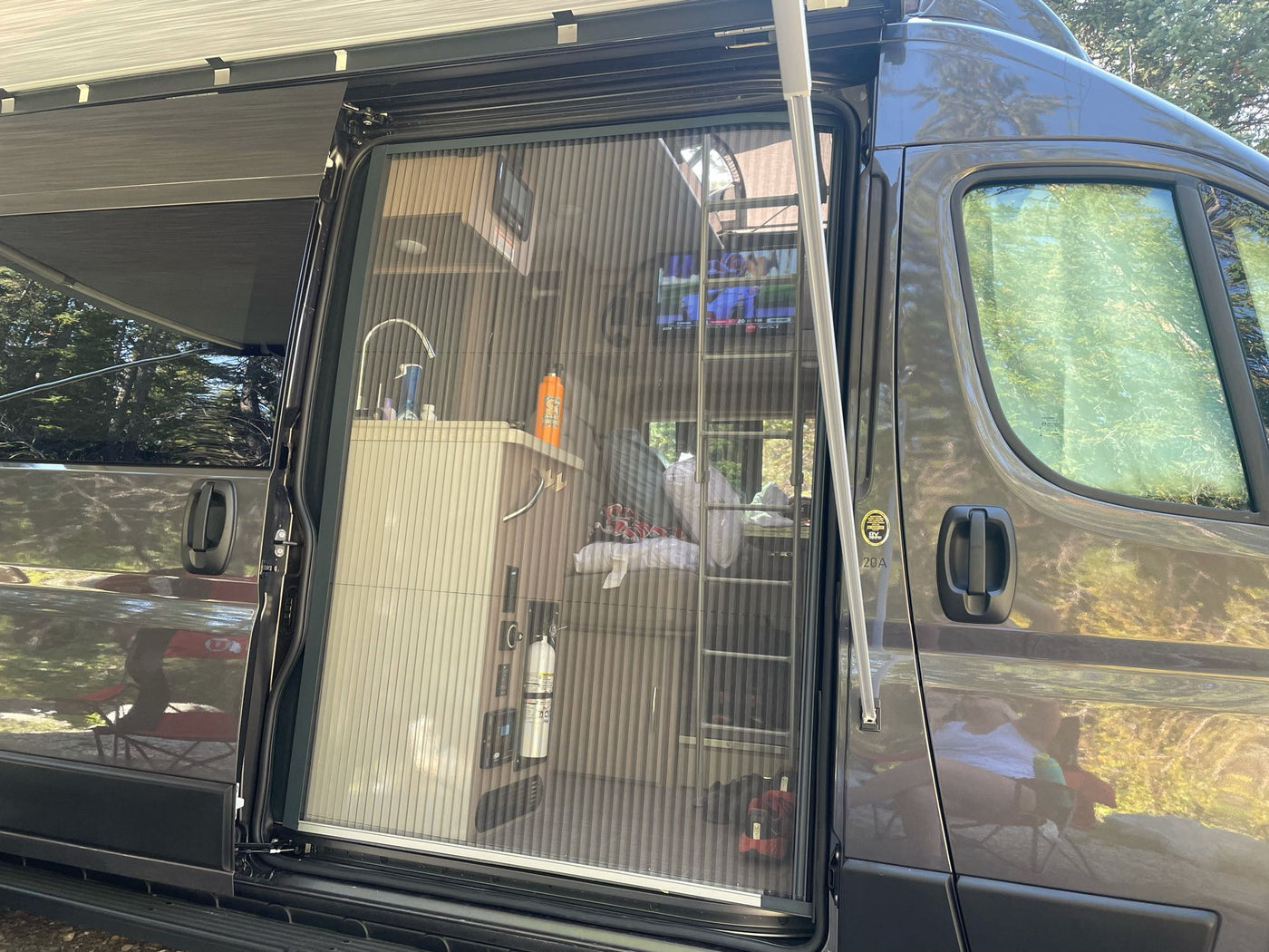 RV rental with side door open & screen extended. Interior visible: kitchen, ladder, TV. Awning provides shade. — photo 5