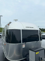 A classic silver Airstream rv rental travel trailer, with dark windows, parked under an overcast sky.