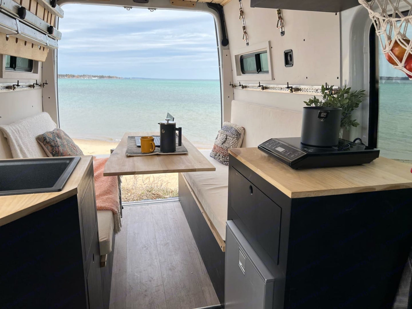  featuring a compact kitchen & dining area.|Stunning RV rental interior with an ocean view. Enjoy a full kitchen & cozy bed in this custom camper van!|White camper van with side door open — photo 2