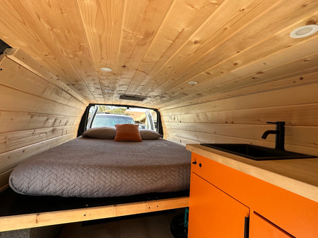 Cozy RV rental interior with wood paneling, comfortable bed, and compact kitchen area.