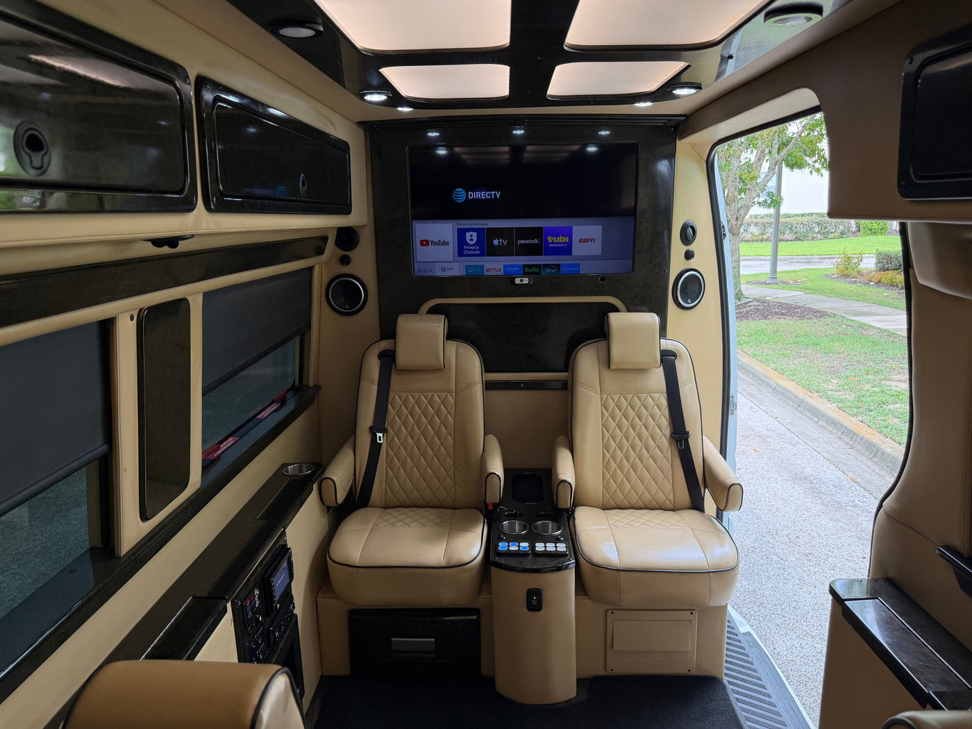 Luxury RV rental interior: two tan leather seats, large screen TV with DIRECTV & apps, comfort controls. Ideal for travel. — photo 11