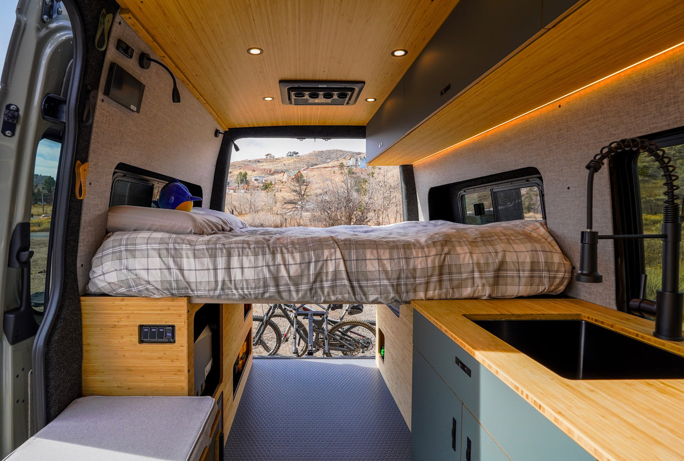 Inside a chic RV rental: bamboo ceiling, comfy bed, kitchen with sink, and bike storage for travel adventures.