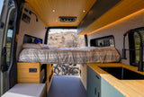 Inside a chic RV rental: bamboo ceiling, comfy bed, kitchen with sink, and bike storage for travel adventures.