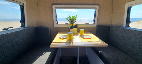 Enjoy beach views from your RV rental: a cozy dining area with two place settings, a flower vase, and ocean scenery.